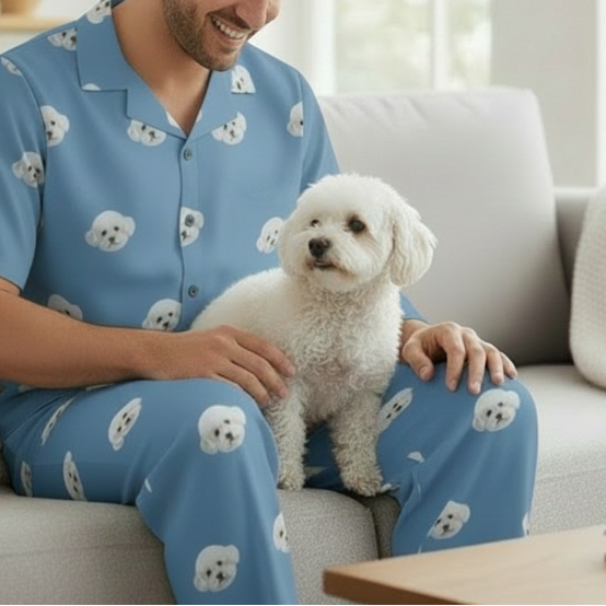 Man in blue pajamas with dog patterns sitting on a couch with a small white dog.