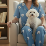 Woman in blue pajamas with dog patterns sitting on a couch with a small white dog.