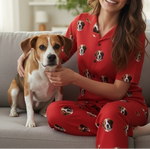 Woman in red pajamas with dog pattern sitting on a couch with a dog.