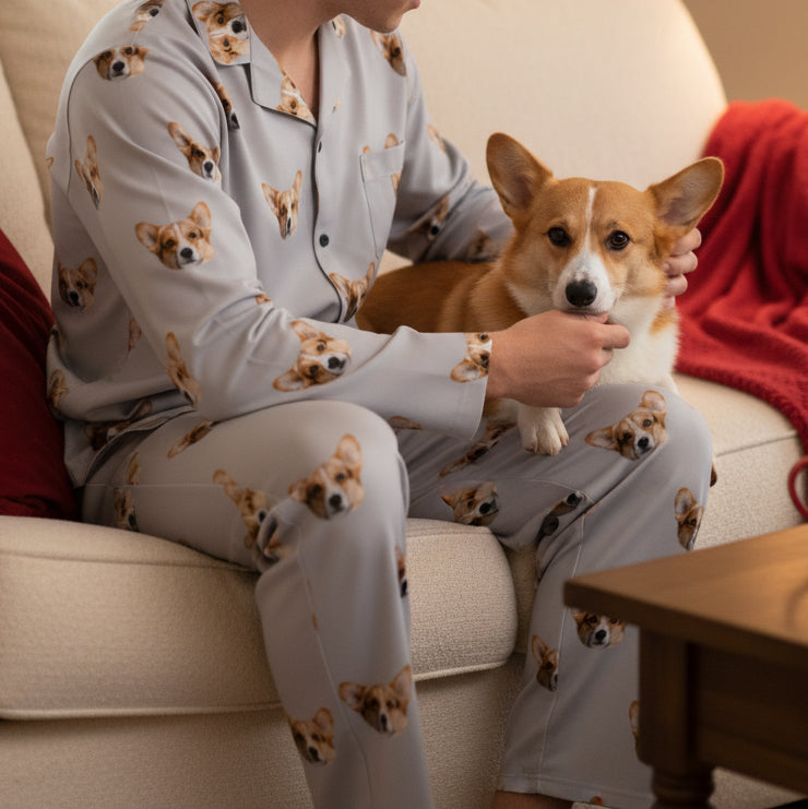 Person wearing dog-patterned pajamas sitting on a couch with a corgi dog.