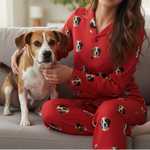 Woman in red pajamas with dog pattern sitting on a couch with a dog.