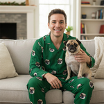 Man wearing green pajamas with dog patterns, holding a pug, in a living room.