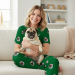 Woman wearing green pajamas with pug prints, holding a pug, sitting on a couch in a cozy living room.